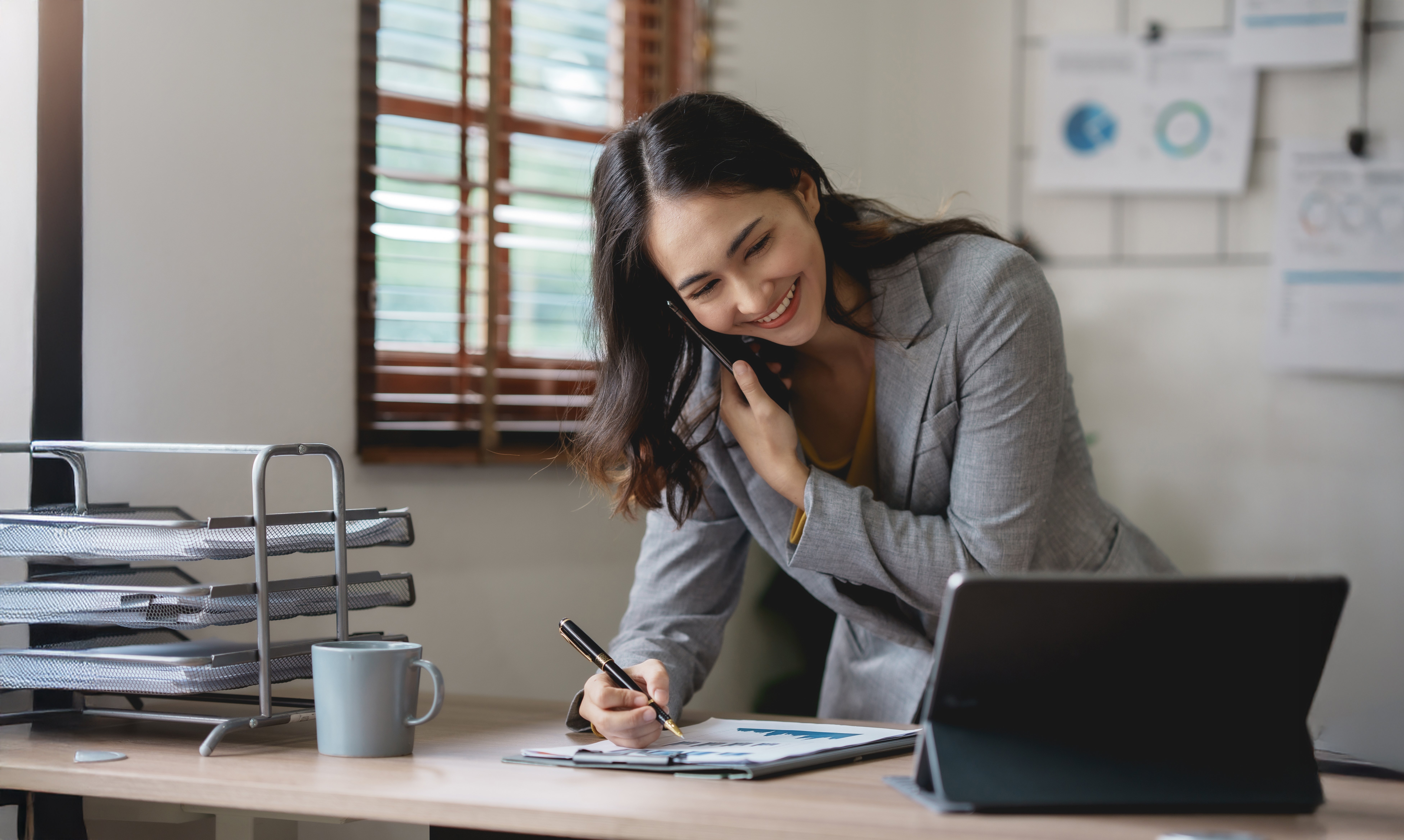 A woman on the phone while writing on a note pad.